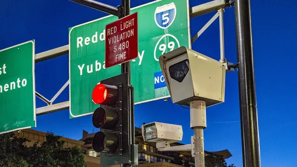 White box with traffic camera at stoplight with green freeway signs for Northern California towns visible in background.