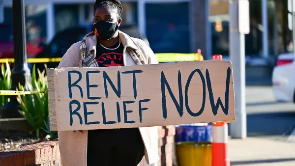 Person holding sign reading 'Rent Relief Now!' wearing blue face mask.