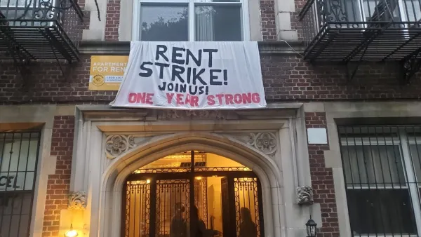 "Rent Strike - Join Us! One Year Strong" cloth banner hanging on red brick New York City apartment building.