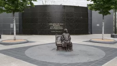 Bronze statue of Rosa Parks sitting on bus bench in center of plaza by Dallas transit station.