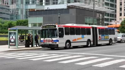 A bus stop in Philadelphia, where people wait under a glass shelter for a bus as it arrives.