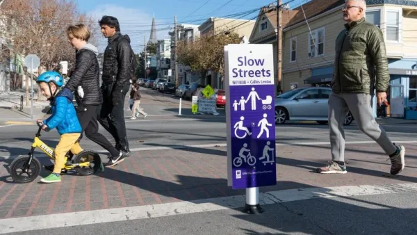 White and purple sign for Slow Street in San Francisco, California with people crossing crosswalk.