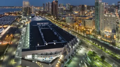 The San Diego Convention Center is illuminated at night with the backdrop of public transit lines and high-rise buildings.