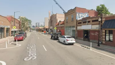 A view up Santa Fe Drive in Denver. Stores and construction are visible along the street, and Downtown Denver looms in the background.
