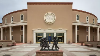 The New Mexico State Capitol building, with a statue of small children playing in the foreground.