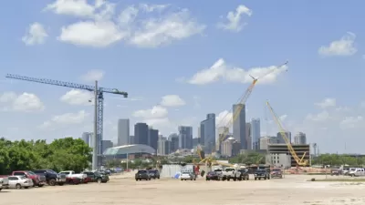 Dirt lot with construction cranes and parked cars with downtown Houston skyline in background