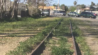 Old railroad line overgrown with grass with cars parked in background