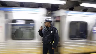 Transit police officer standing on subway platform with blurred train passing behind him.