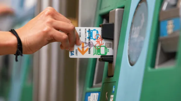 Close-up of hand inserting Mobility Wallet card into green Los Angeles Metro ticketing machine.