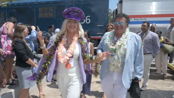 Blonde woman in sequined purple hat walking away from Amtrak train smiling at camera with other people behind her.