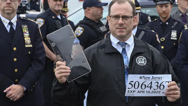 New York City police official holding up paper license plate and clear cover at press conference.