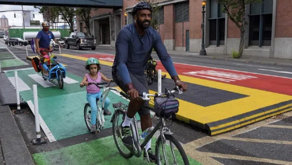 Dad and small kids ride bikes on colorful bike lane next to bus lane protected with low buffers in Portland, Oregio.