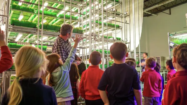 Man showing tour group of children indoor farming with automated planting shelves.