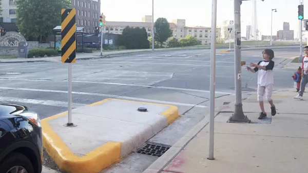 Two children stand on sidewalk at crosswalk with yellow curb extension.