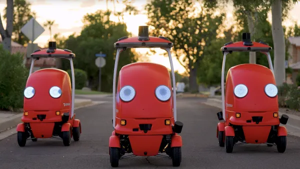 Three red DoorDash delivery robots facing camera on suburban street.