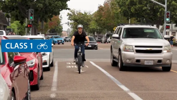Man wearing helmet rides e-bike in separate bike lane in Carlsbad, California net to white SUV.