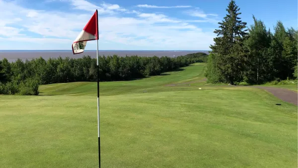 Golf course green with red flag in foreground against a bright blue sky in Duluth, Minnesota.