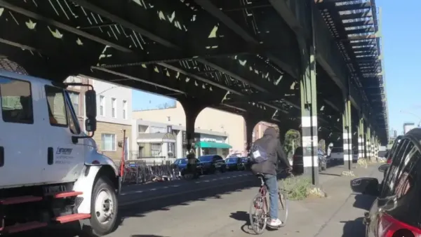 Cyclist rides along 31st street in New York City next to elevated train track.