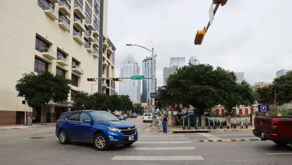 Blue SUV turning left in intersection in Austin, Texas with pedestrians waiting to cross and Lime scooters lined up on sidewalk.