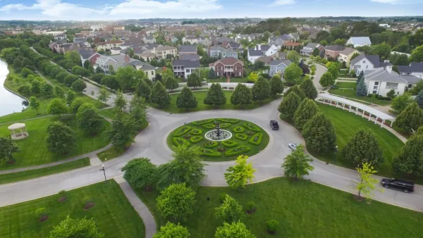 Roundabout with green space and statue in middle nedt to dense cluser of mid-rise housing in Carmel, Indiana.