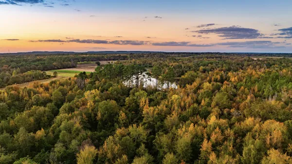 An aerial view of the new state park, with a forest and lake visible under a sunset.