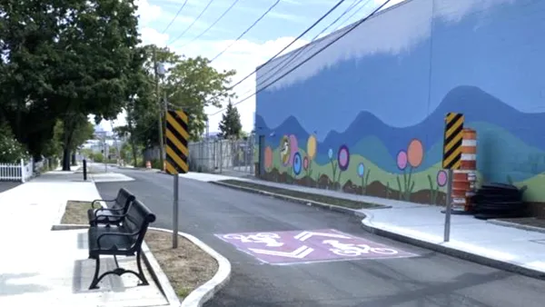 A narrow road with signs for bike lanes with a mural of flowers in the background.