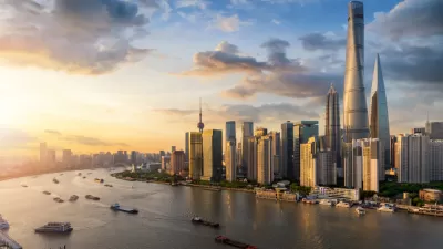 A view of Downtown Shanghai's skyscrapers, rising above a Huangpu River full of boats leaving wakes visible in the fading light of sunset.
