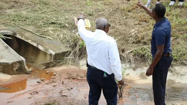 Two men in collared shirts and slacks looking and pointing at drainage ditch.