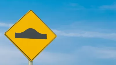 A yellow sign street sign showing the symbol for a speed bump: a simple black bump.