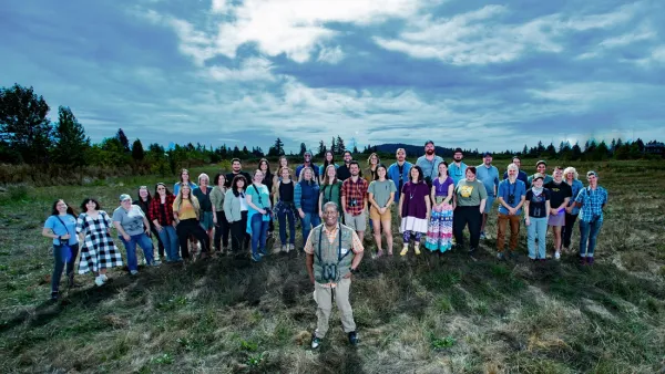 A crowd of people look up at a camera on the field that will become a nature sanctuary.
