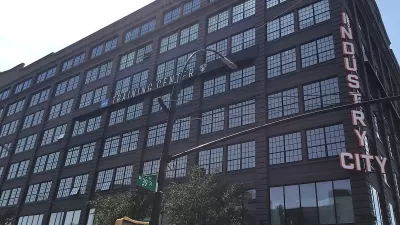 Looking up at black multi-story building with Industry City neon sign on corner.