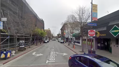 A narrow, one-way street is lined with businesses.