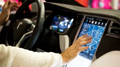 The interior of a Tesla, with a large video screen. The person behind the wheel is touching the screen.