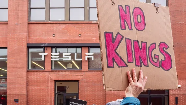 Close-up on cardboard sign reading 'No Kings' being held up at protest at Tesla offices in Brooklyn, New York.