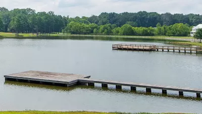 View of docks on lake surrounded by green trees and lawns with one white house at right