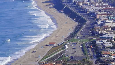A parking lots and homes sit on a bluff above a large beach on Pacific coast in Southern California.