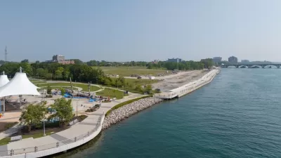 Aerial view of Uniroyal Promenade site on East Riverfront in Detroit with wide paved walkway along river and shaded pavilion at left.