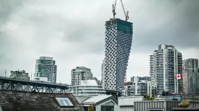 View of Vancouver House skycraper under construction with two cranes at top and other downtown Vancouver buildings surrounding it against a grey sky