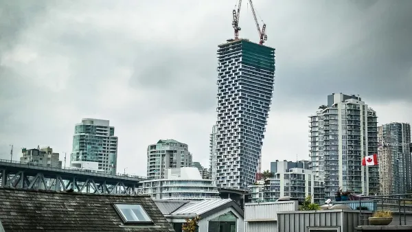 View of Vancouver House skycraper under construction with two cranes at top and other downtown Vancouver buildings surrounding it against a grey sky