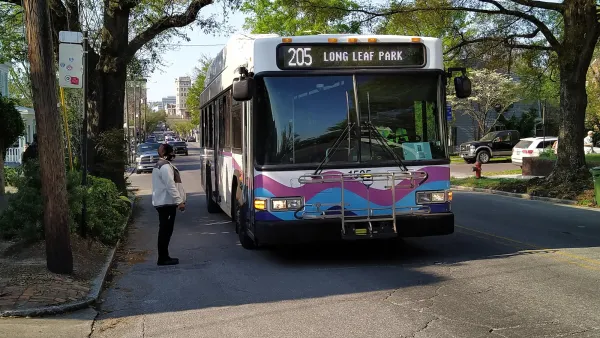 Person waits to board white bus with purple and blue wave graphic across front at a bus stop in Wilmington, Delaware.