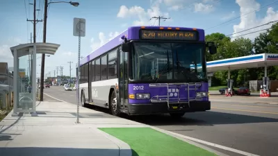 Purple buss pulls up to bus stop in green bus lane.