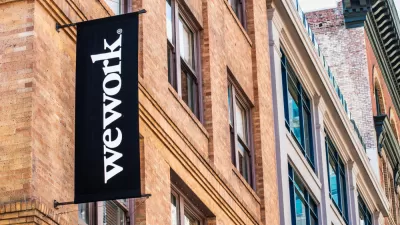 The sign for a WeWork office appears at the exterior of a brick high-rise in a dense downtown.