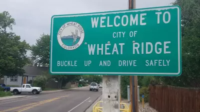 A road sign reads "Welcome to City of Wheat Ridge Buckle Up and Drive Safely"