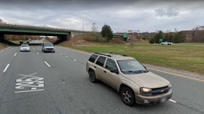 A two-lane highway cuts through a small canyon. The photo is taken from the perspective of a vehicle on the road.