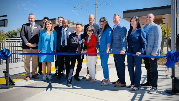 A group of smiling people cut a blue ribbon in front of Sacramento's new light rail station.