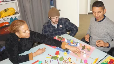 Three people gather around a table to discuss maps made of toys and found objects.