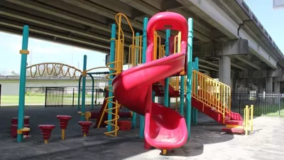 Red, yellow, and green plastic playground equipment in small park under Claiborne Expressway overpass in New Orleans, Louisiana.