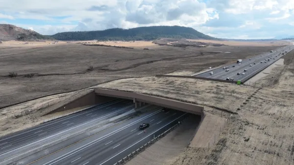 The largest wildlife overpass in North America stretching over the I-25. Both sides of the overpass, and the overpass itself, are covered in brown grass.
