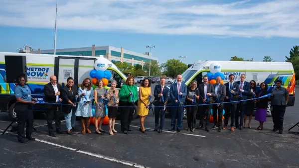 A crowd of people in front of two MetroNow buses, cutting a blue ribbon.