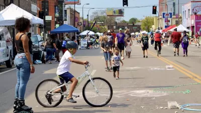 Diverse people of all ages walking and biking at Minneapolis Open Streets event with temporary festival booths along the sides of the street